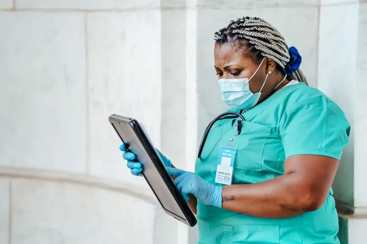 Enfermera revisando datos de monitorización remota de pacientes en pantalla digital de hospital
