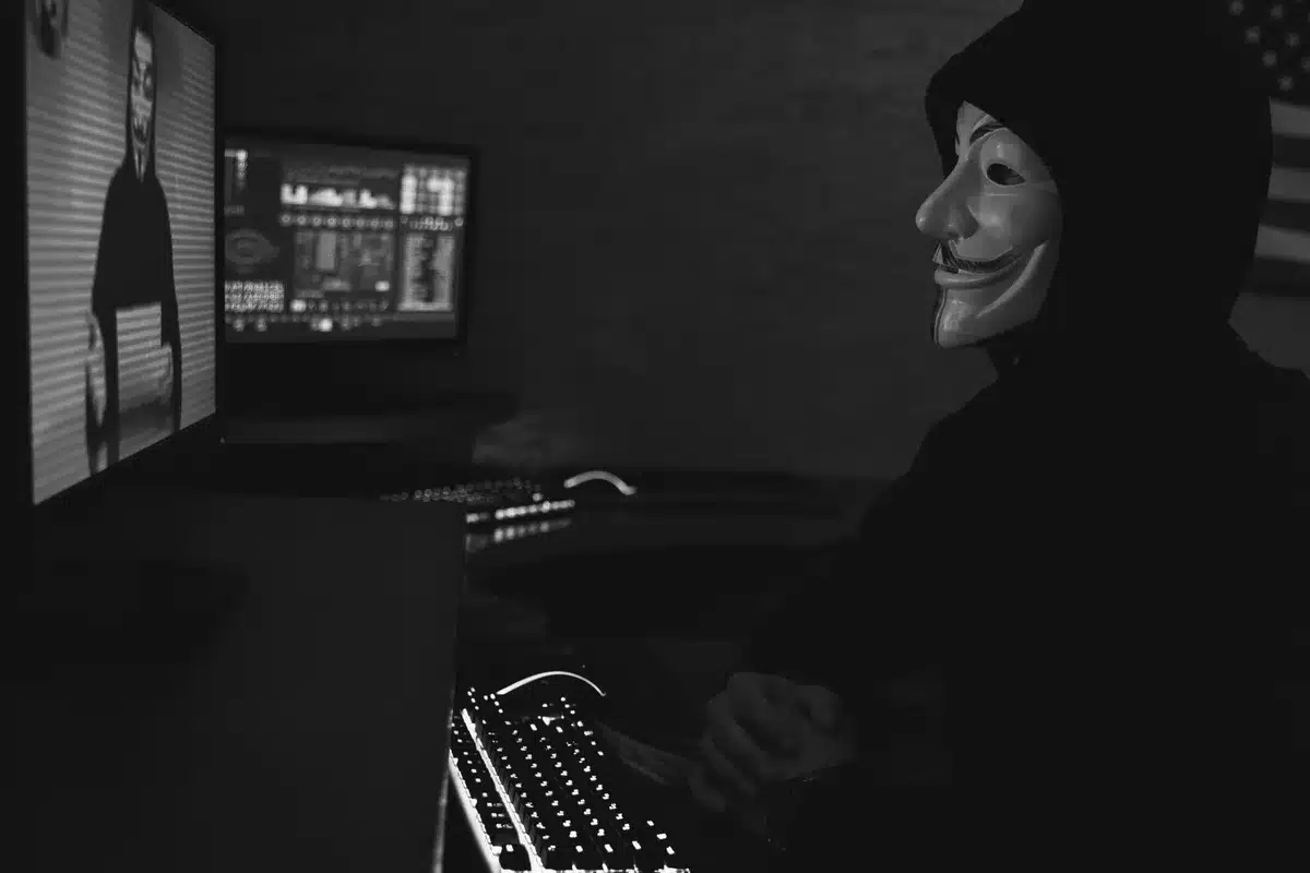 Persona anónima frente a pantalla de computadora en ambiente oscuro, símbolos de código visible