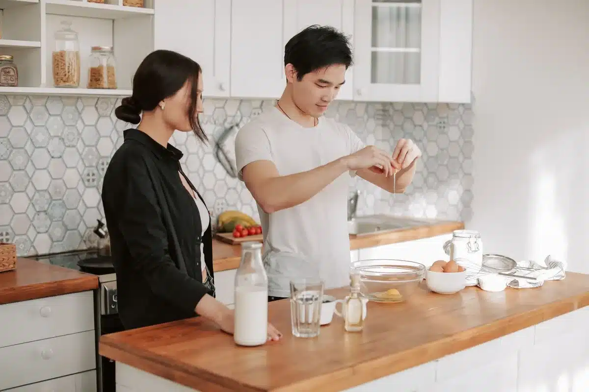 Manos rompiendo un huevo en un bol sobre una encimera de cocina con verduras de fondo