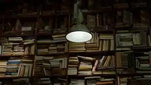Libros de terror apilados en una mesa con luz de velas proyectando sombras en la biblioteca