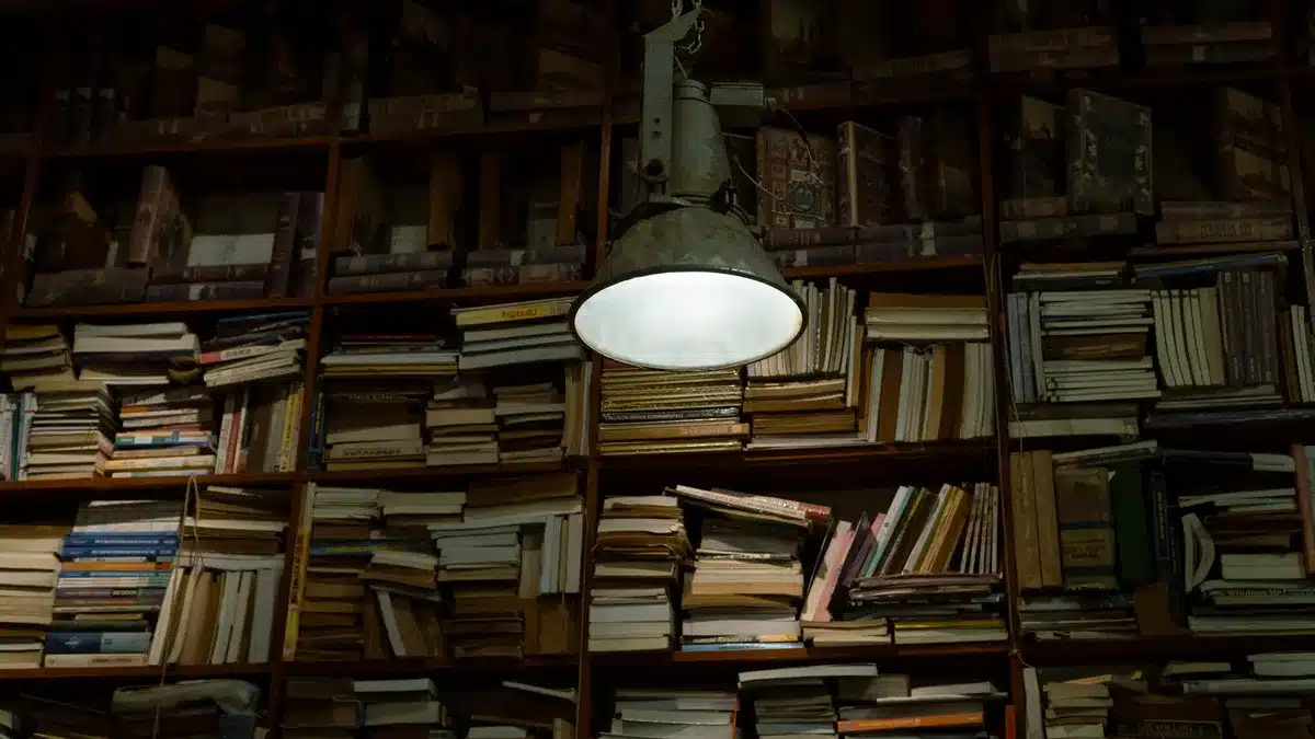Libros de terror apilados en una mesa con luz de velas proyectando sombras en la biblioteca