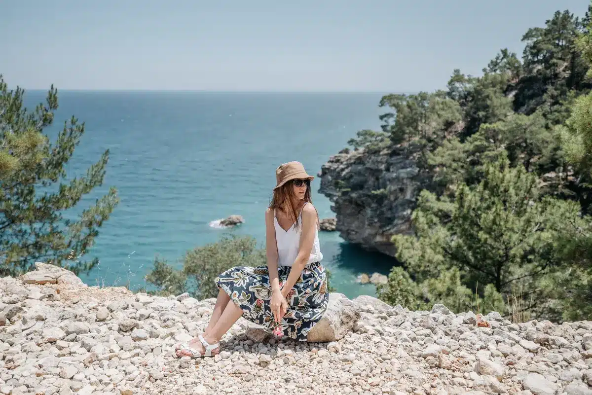 Maleta de verano con ropa clara, bolso de rafia y accesorios minimalistas listos para un viaje al Mediterráneo