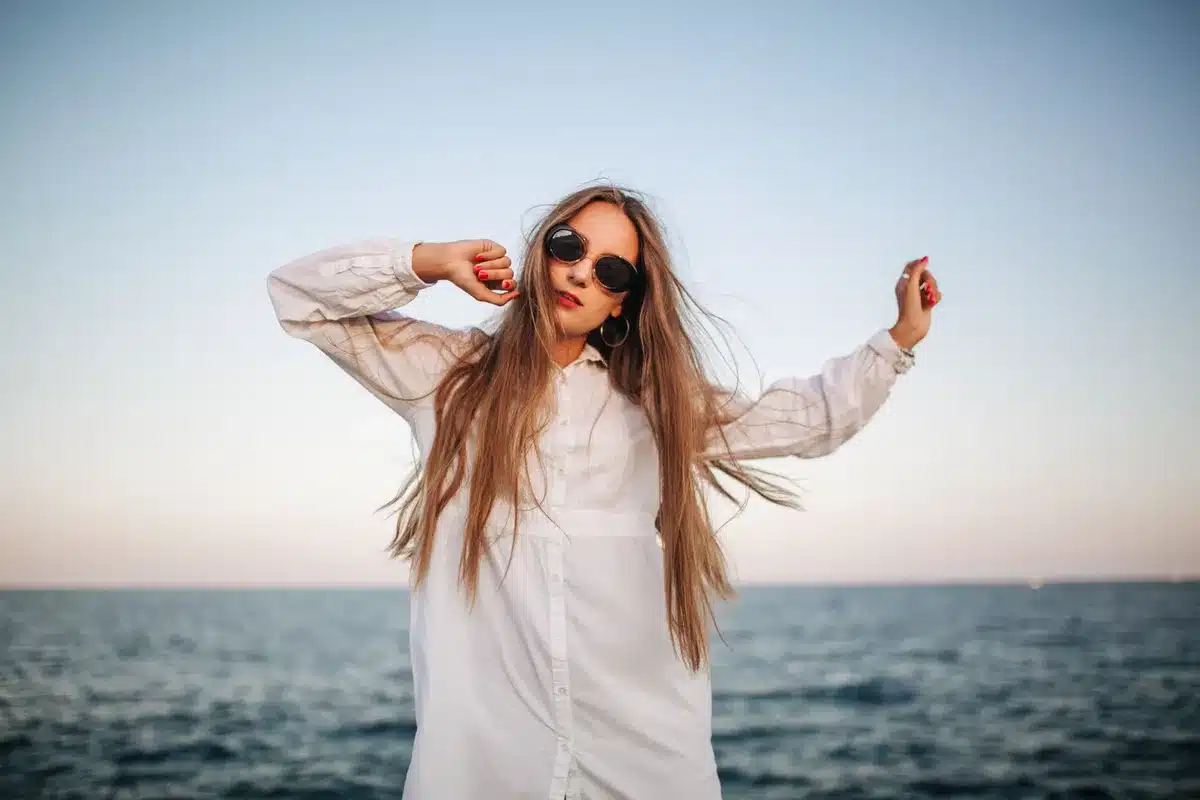 Mujer con vestido blanco fluido caminando en la playa al atardecer