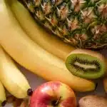 Mano anónima eligiendo entre refresco light y fruta fresca en una cocina
