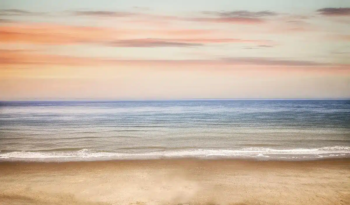 Playa mediterránea con aguas tranquilas y luz dorada de septiembre, con pocos visitantes disfrutando del mar.