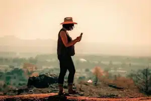 Manos sosteniendo un iPhone sobre una mochila de senderismo con cielo amplio al atardecer