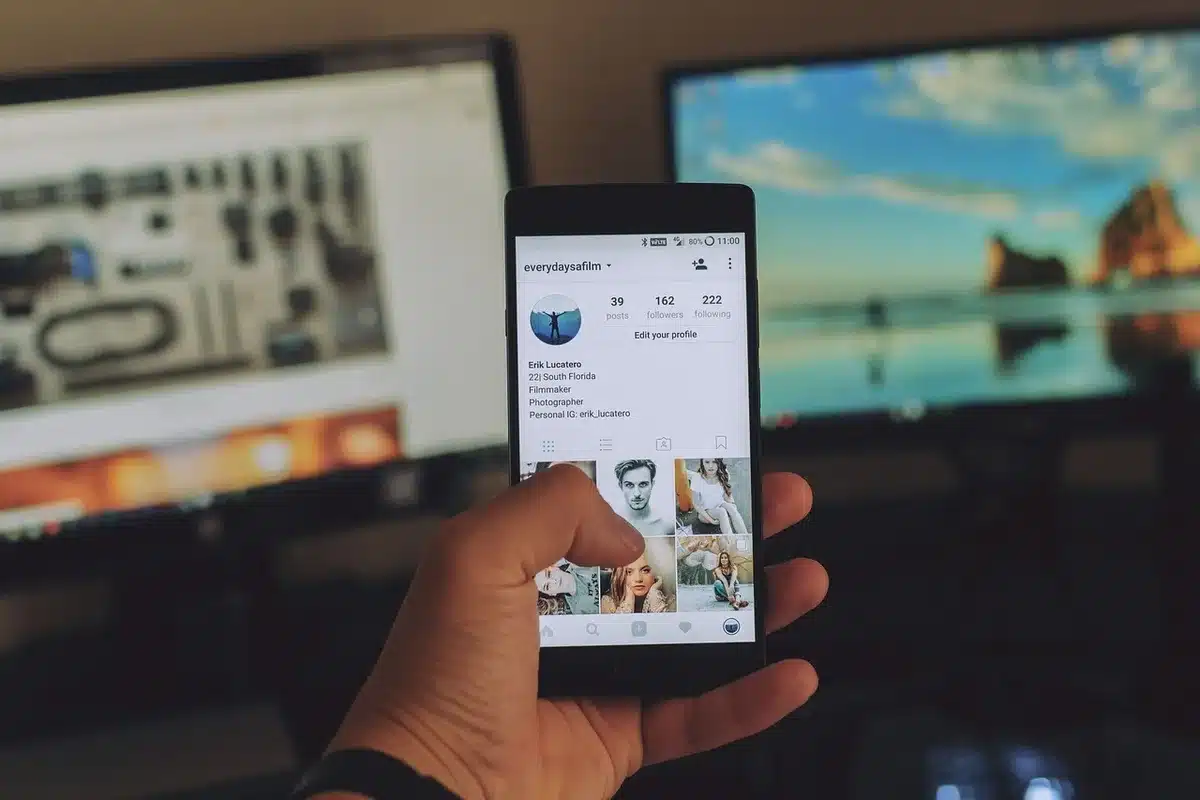 Manos sosteniendo un teléfono inteligente junto a una computadora portátil con carrito de compras en pantalla