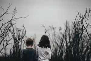 Dos figuras anónimas de espaldas frente a ruinas y arcos bajo cielo nublado