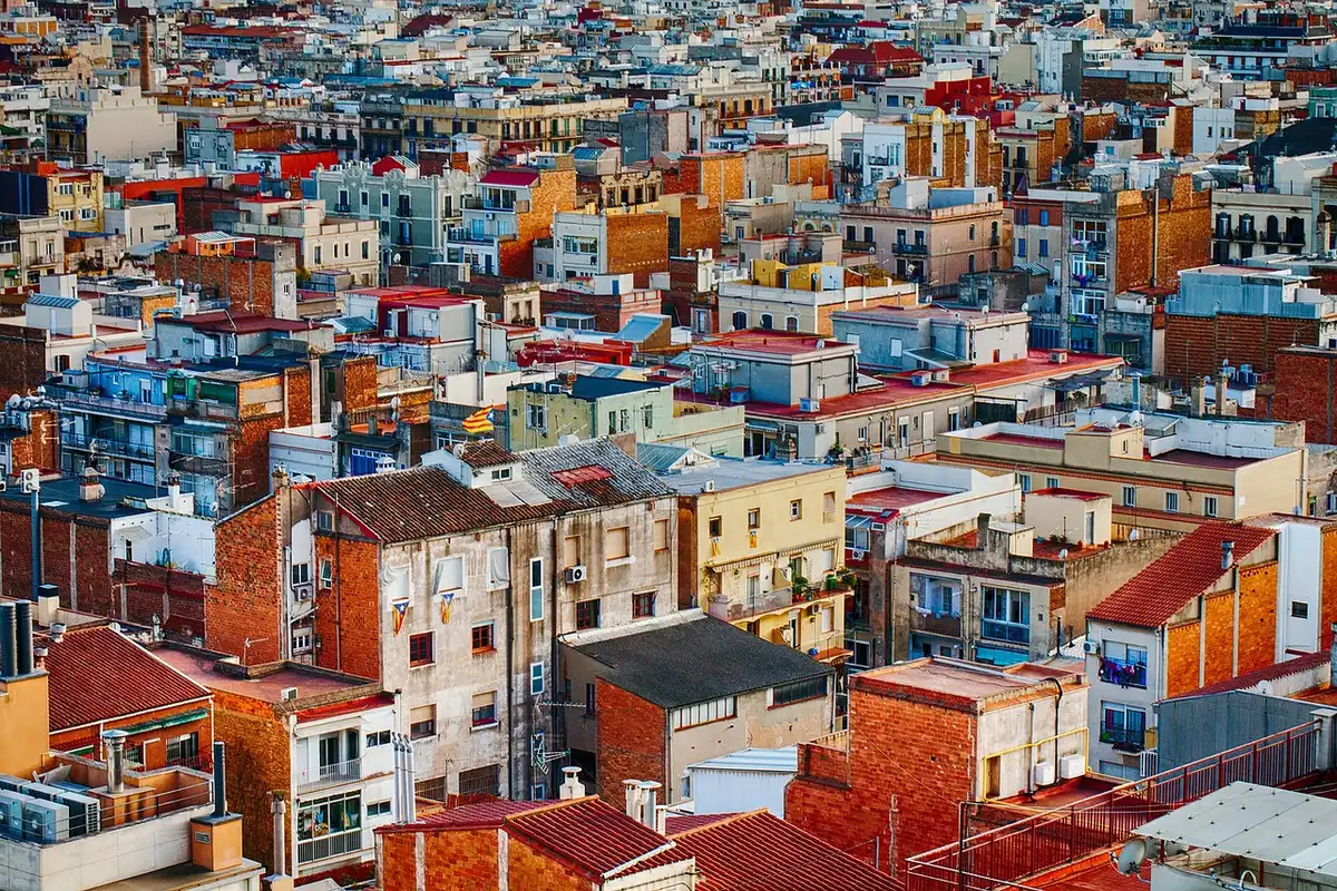 Figura anónima con capa observando una ciudad desde un tejado al anochecer