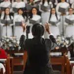 Manos anónimas con smartphones en una sala de concierto, orquesta desenfocada al fondo
