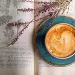 Manos con taza de café junto a prendas de otoño colgadas en un perchero